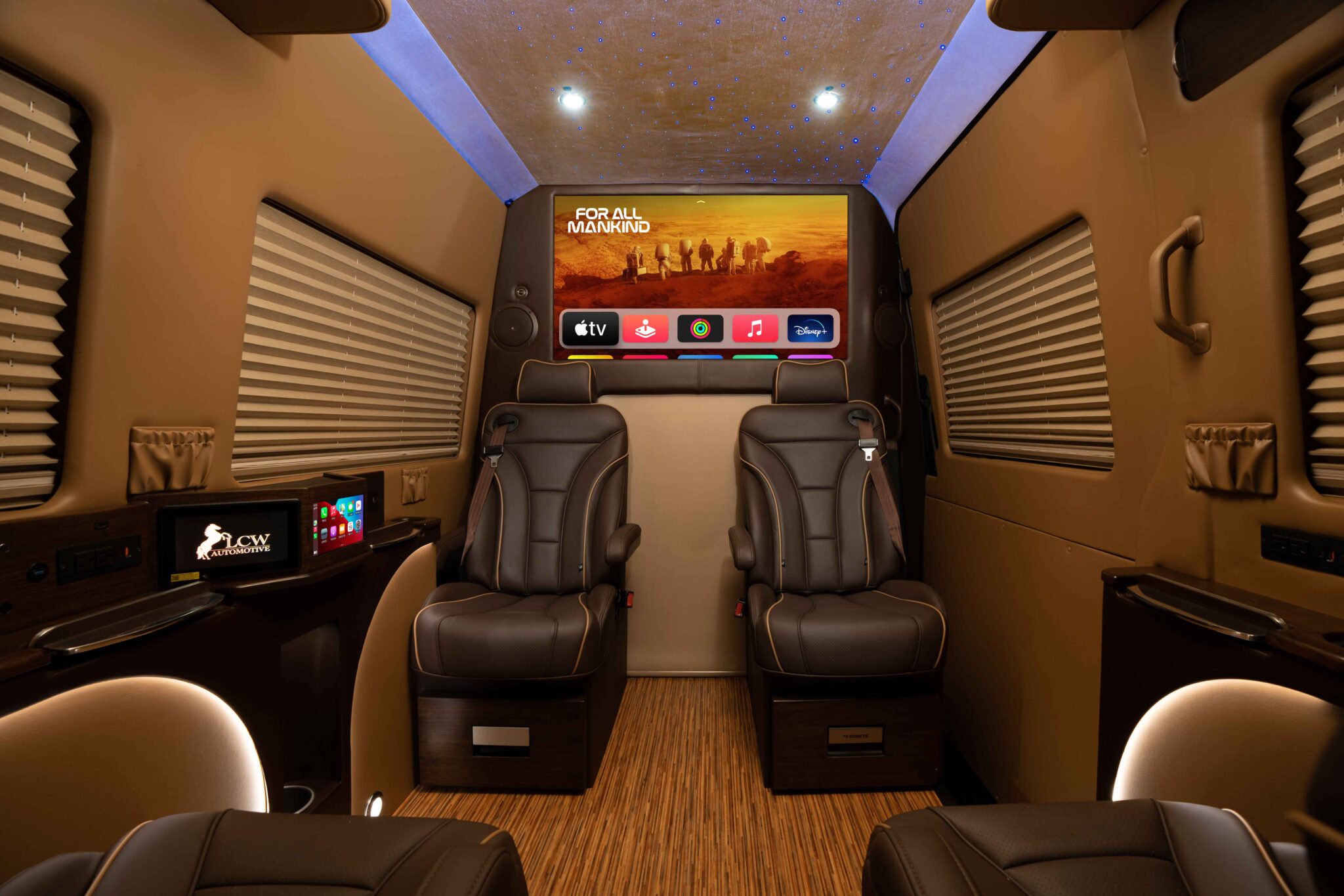 Custom sprinter van interior with leather captain’s chairs, ambient lighting, and a widescreen TV.